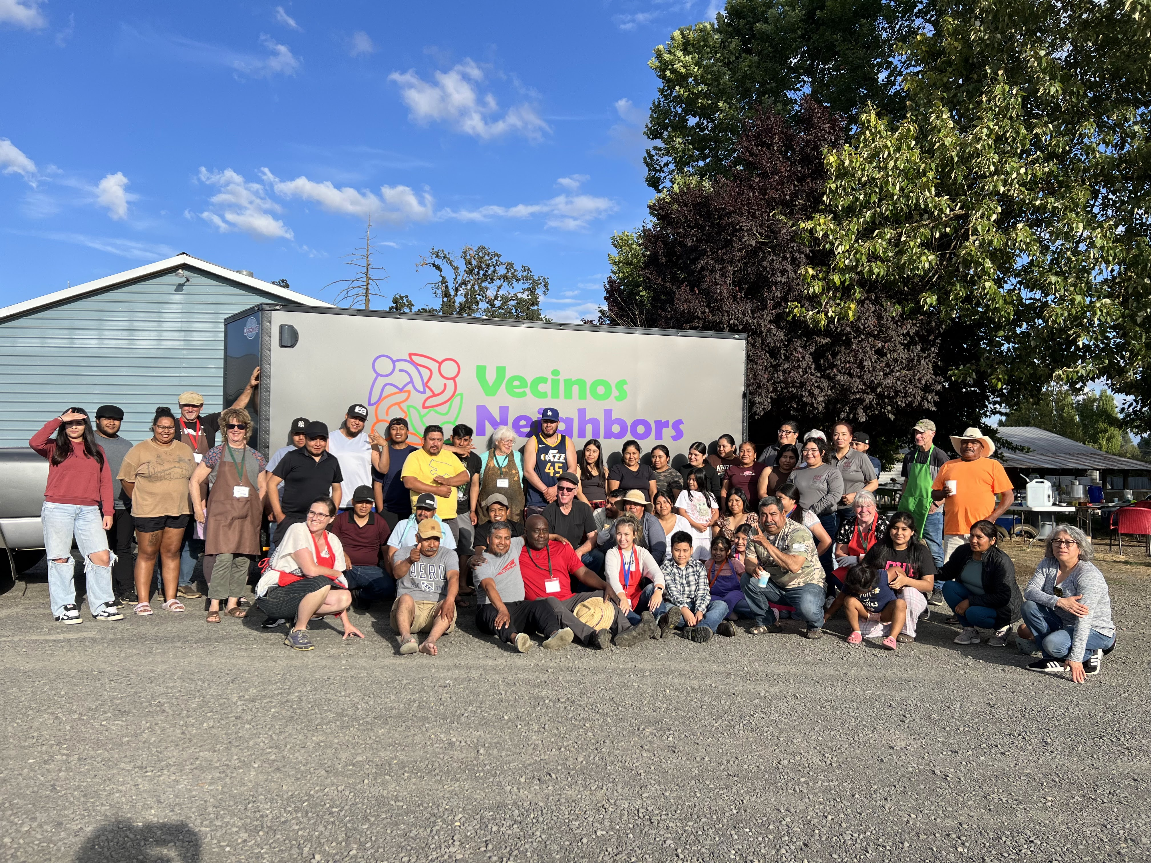Picture of a bunch of Vecinos Neighbors volunteers in front of a trailer in the sunshine.